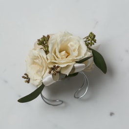 Ivory rose wrist corsage with white ribbon on a silver cuff bracelet.