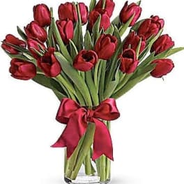 Arrangement of red tulips in a clear glass vase with a red ribbon bow