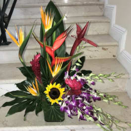 Tall tropical arrangement with birds of paradise, sunflower, and purple orchids in a green vase