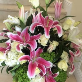 Large arrangement of pink lilies, white roses, and hydrangeas in a low container