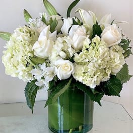 White roses, lilies, and hydrangeas arranged in a clear glass cylinder vase