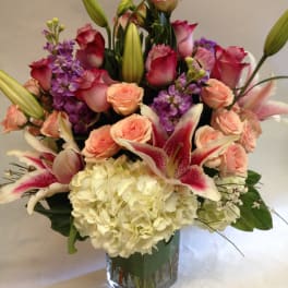 Mixed bouquet of pink roses, lilies, and white hydrangea in a glass vase