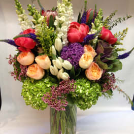 Mixed bouquet in a clear glass vase with pink, peach, white, and purple flowers