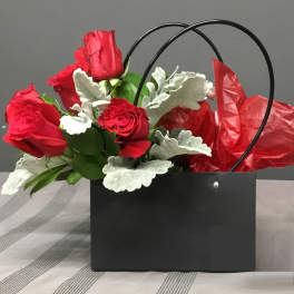 Red roses in a black gift bag with silver foliage and red tissue paper