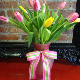 Pink and yellow tulips in a frosted pink vase tied with a striped pink and green ribbon bow.