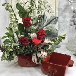 Red roses and white snapdragons in a red ceramic cardinal container beside a matching empty dish.