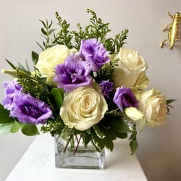 Bouquet of cream roses and purple lisianthus in a clear square vase