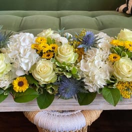 Low floral centerpiece with white roses, hydrangeas, and yellow blooms in a wooden box