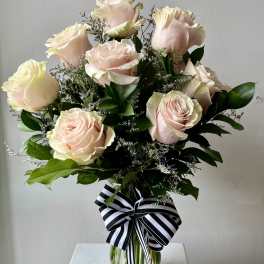 Bouquet of pale pink roses in a clear glass vase with a striped ribbon