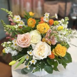 Mixed arrangement of yellow, peach, and white roses with spring blooms in a white vase
