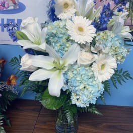 White lilies, gerbera daisies, and blue hydrangeas in a glass vase