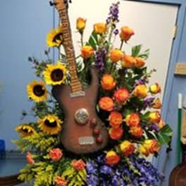 Guitar-shaped floral arrangement with sunflowers, orange roses, and purple flowers