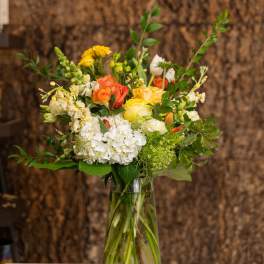 Tall bouquet of yellow and orange roses, white hydrangeas, and mixed flowers in a clear glass vase.