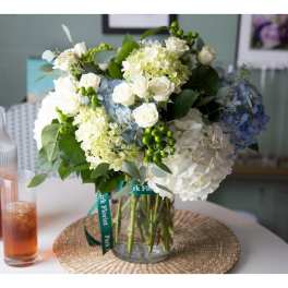 White and blue hydrangeas with white roses arranged in a clear glass cylinder vase