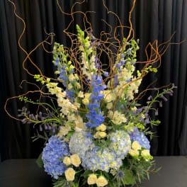 Tall blue and white floral arrangement in a black vase with curly branches