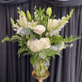 White floral arrangement in a glass vase on a gold pedestal stand