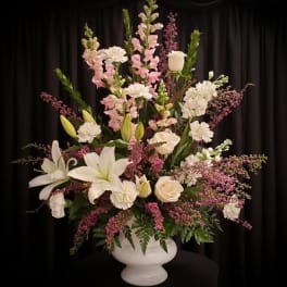 Tall floral arrangement with white lilies, roses, and pink blooms in a white vase