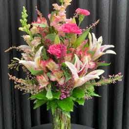 Tall pink and white lily and carnation arrangement with snapdragons in a clear glass vase