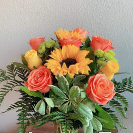 Vase arrangement with orange roses, yellow sunflower and yellow roses with green accents