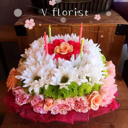 Round floral cake of white daisies, pink carnations, roses, and green mums topped with striped candles.