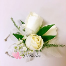 White rose wrist corsage with small white filler flowers and sheer ribbon on a silver cuff.