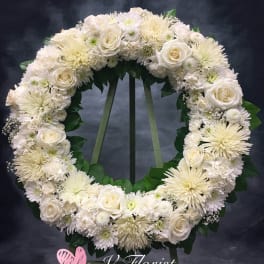 Large white rose and chrysanthemum wreath on a stand against a dark background