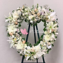 Large white and pale peach floral wreath on a stand against a light wall