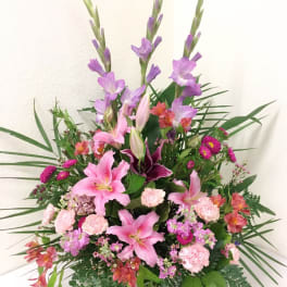 Tall pink and purple mixed flower arrangement with lilies and carnations in a fan-shaped design