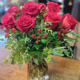 Red roses arranged in a clear glass vase with berry accents