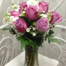 Pink and lavender roses arranged in a clear glass vase with white filler flowers.