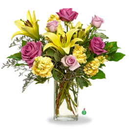 Arrangement of yellow lilies, yellow carnations, and lavender roses in a clear glass vase