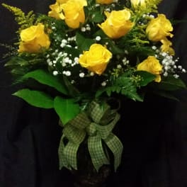 Yellow roses arranged in a glass vase with a green ribbon