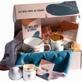 Get well gift box with mug, body products, towel, socks, and bath items arranged in pink packaging.