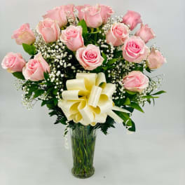 Pink rose bouquet in a clear glass vase with a cream ribbon bow