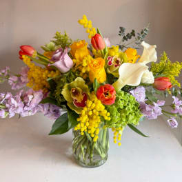 Bright mixed bouquet with yellow roses, red tulips, white calla lilies, orchids and stock in a clear glass vase