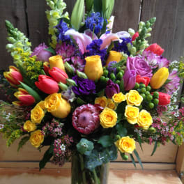 Colorful mixed bouquet in a clear glass vase with roses, tulips, lilies, and snapdragons