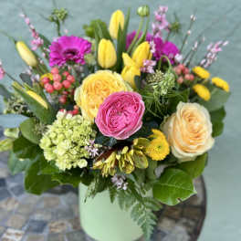 Mixed bouquet of yellow tulips, pink gerberas, roses, and hydrangea in a light green vase