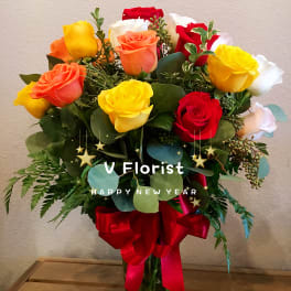 Tall glass vase of mixed red, yellow, orange, and white roses tied with a red bow