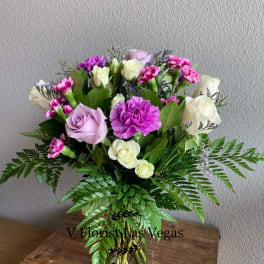Mixed bouquet of lavender roses, white roses, and purple carnations in a clear glass vase