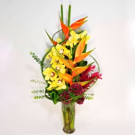 Tall tropical bouquet with orange heliconia and yellow orchids in a glass vase