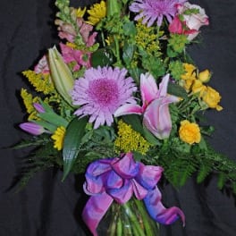 Mixed bouquet with pink lilies, purple daisies, and yellow flowers in a glass vase