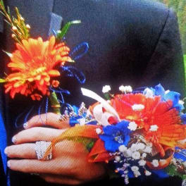 Person holding two colorful floral corsages with orange and blue flowers