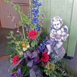 Tall mixed flower arrangement with a cherub statue and purple ribbon