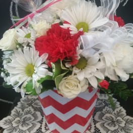 Bouquet of white daisies, red carnations, and white roses in a chevron vase with a heart topper