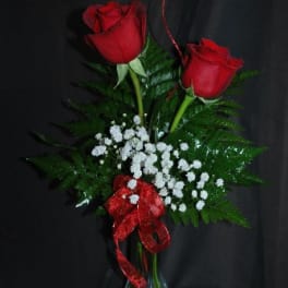 Two red roses in a clear glass vase with baby's breath and a red ribbon
