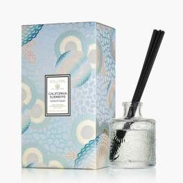 Reed diffuser in a glass bottle beside a patterned box