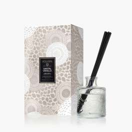 Glass reed diffuser with black reeds beside a patterned box