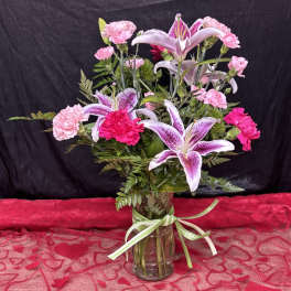 Pink carnations and lilies arranged in a glass vase with a ribbon.