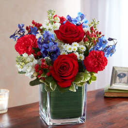 Red, white, and blue mixed flower arrangement in a square glass vase