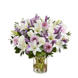 Arrangement of white lilies, white roses, and lavender flowers in a clear glass cylinder vase